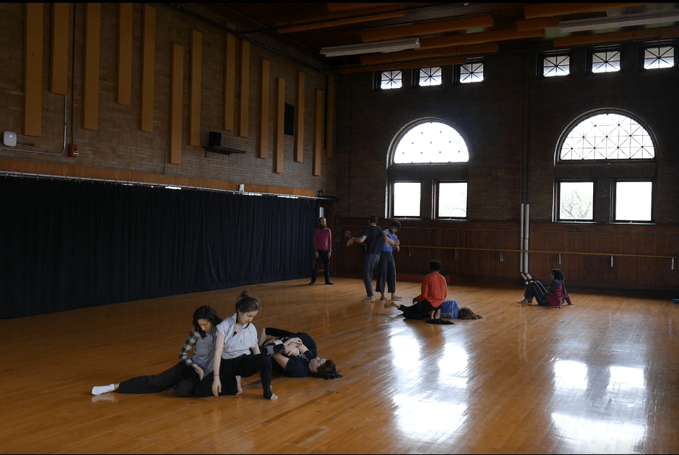 several people doing contact improv in a large room with wooden floor
